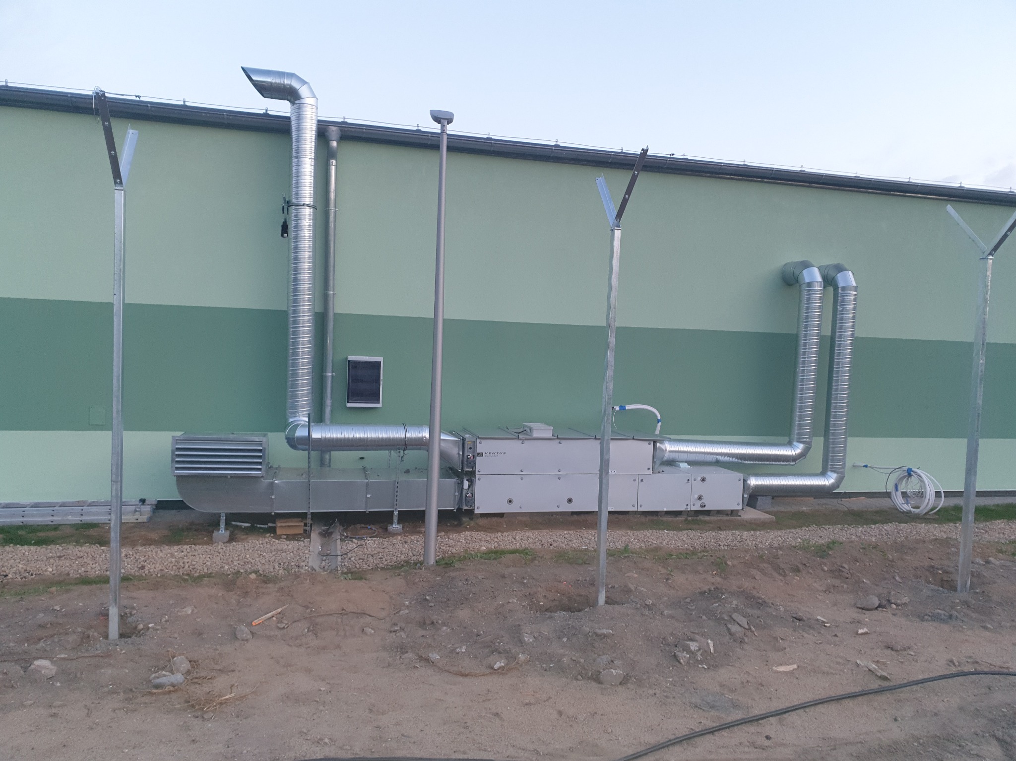 Montaż rekuperacji w budynku komercyjnym w Pile. Widoczne kanały wentylacyjne i centrala rekuperacyjna na zewnątrz budynku z zieloną elewacją.