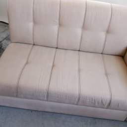 Kacper Bakuła Diamond Professional Cleaning - Jasnobeżowa, dwuosobowa kanapa z pikowanym oparciem i charakterystycznymi pionowymi przeszyciami, ustawiona na szarym dywanie.