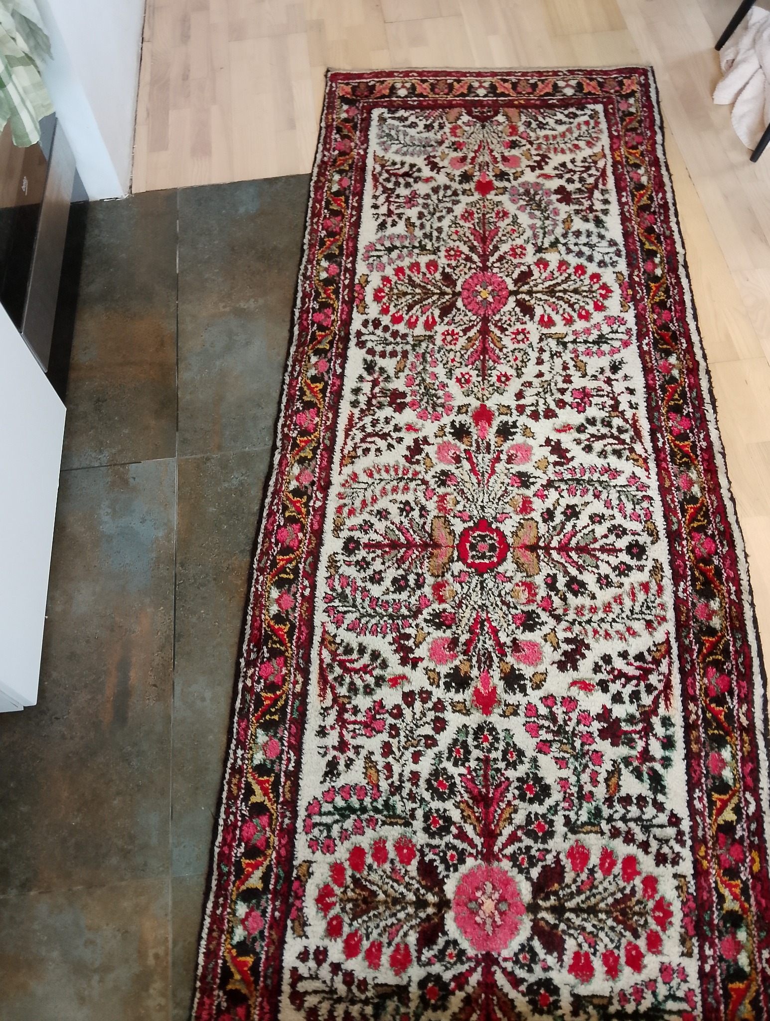 Długi, wąski dywan w orientalne wzory, leżący na styku płytek podłogowych i drewnianej podłogi.