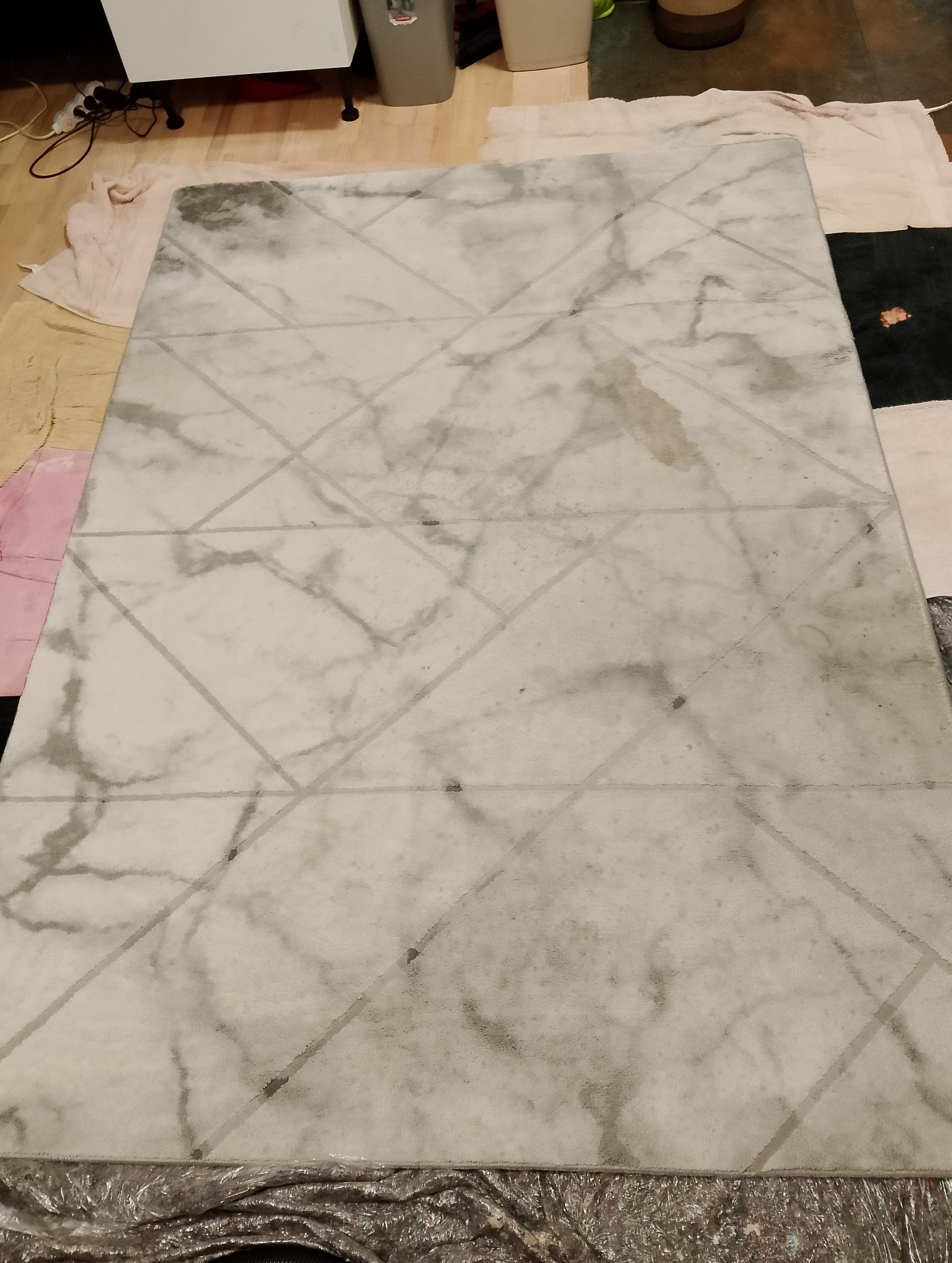 Marmurkowy dywan geometryczny, częściowo pokryty pianą czyszczącą, leżący na podłodze zabezpieczonej ręcznikami i folią.