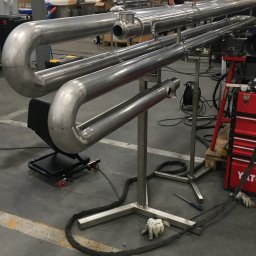 K.K.W. Krzysztof Kotlarz - Konstrukcja z rur nierdzewnych na metalowym stelażu w warsztacie, widoczne ślady obróbki i spawania, narzędzia i akcesoria w tle.