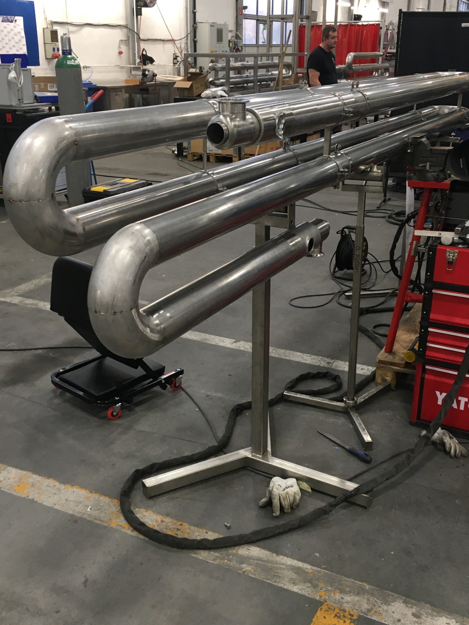 Konstrukcja z rur nierdzewnych na metalowym stelażu w warsztacie, widoczne ślady obróbki i spawania, narzędzia i akcesoria w tle.