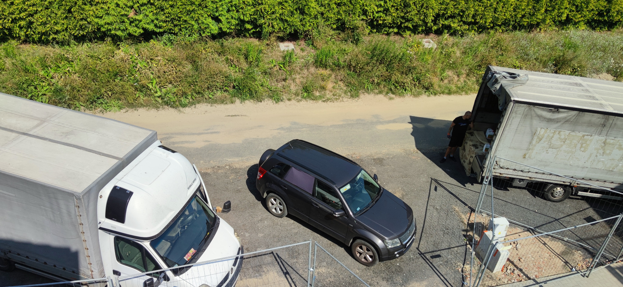 Dwa busy dostawcze zaparkowane obok ciemnoszarego samochodu osobowego, z pracownikiem przy otwartych drzwiach jednego z busów, widok z góry.