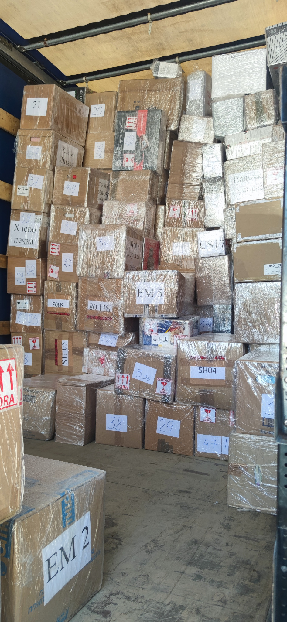Wnętrze busa wypełnione kartonami różnej wielkości, zabezpieczonymi folią stretch, niektóre z etykietami z numerami i napisami w języku polskim i rosyjskim.
