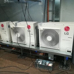 EKOCERT SPÓŁKA Z OGRANICZONĄ ODPOWIEDZIALNOŚCIĄ - Trzy zewnętrzne jednostki klimatyzacji LG Smart Inverter zamontowane na metalowej konstrukcji, obok butla z gazem, skrzynka z narzędziami, widoczne kable i instalacje.