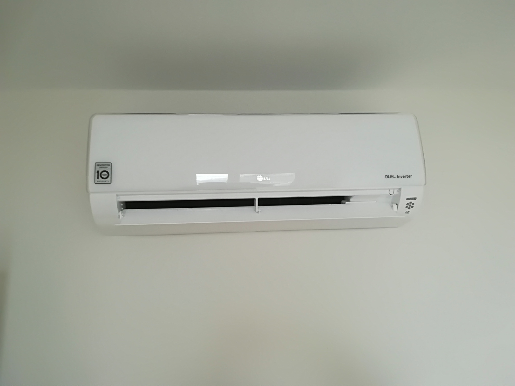 Biała klimatyzacja LG Dual Inverter zamontowana na jasnej ścianie, widoczne logo i oznaczenie 10-letniej gwarancji na sprężarkę.