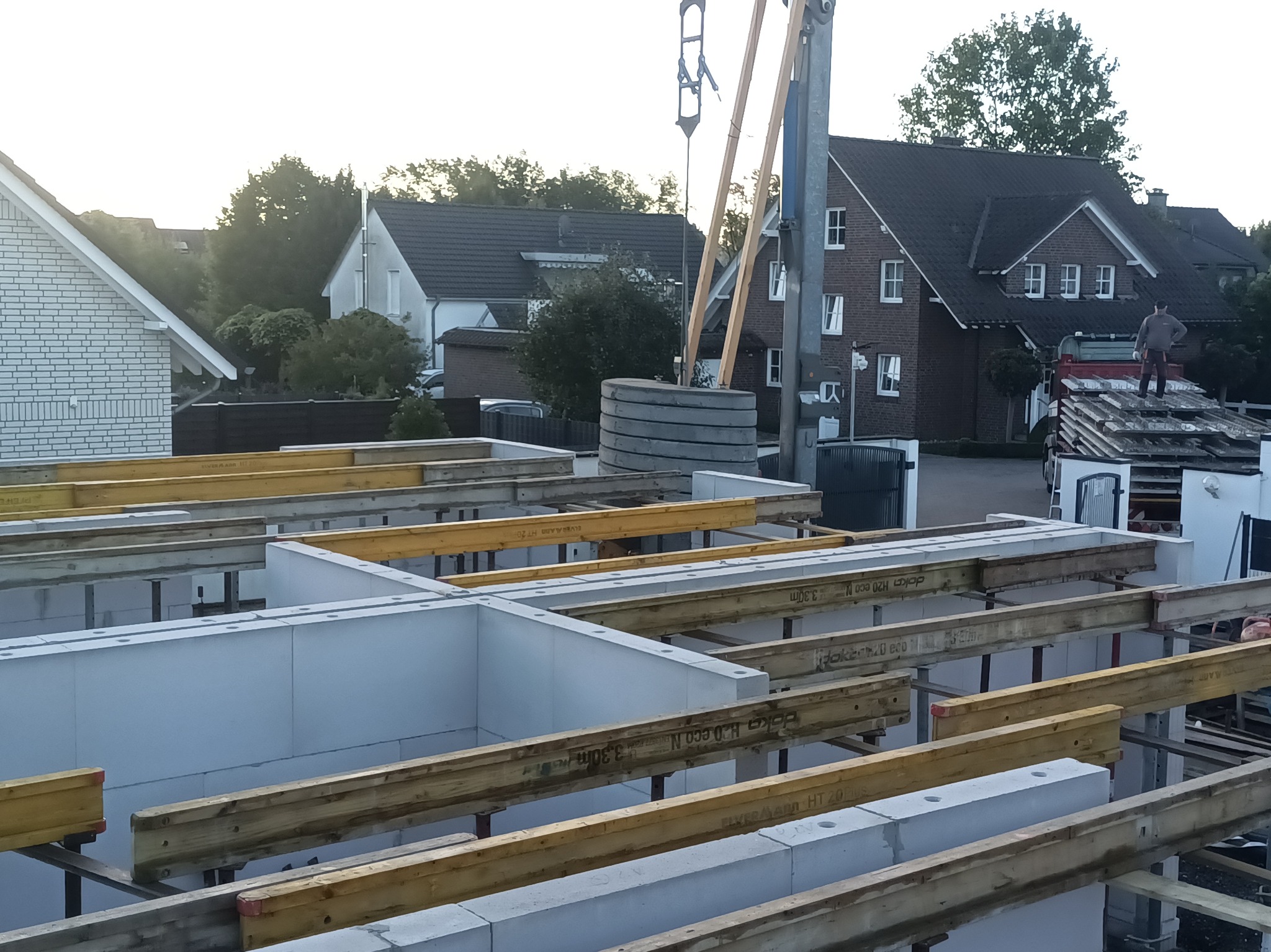 Fundamenty domu jednorodzinnego w trakcie budowy, widoczne szalunki i bloczki fundamentowe, w tle zabudowa mieszkalna i dźwig budowlany.