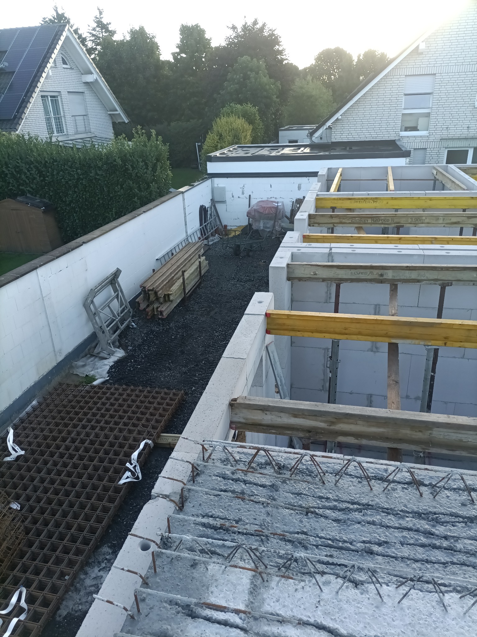 Budowa domu: widok z góry na fundamenty, ściany z bloczków i zbrojenie stropu. Widoczne podpory i materiały budowlane. Ujęcie z góry, w tle zabudowa jednorodzinna.