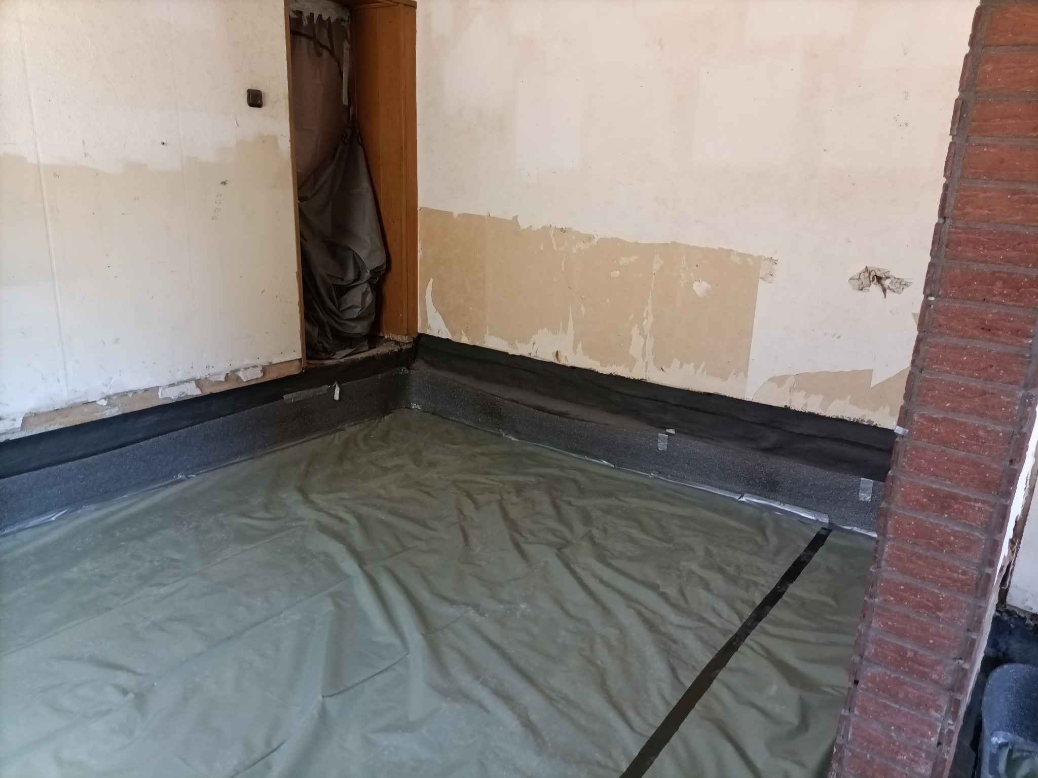 Przygotowanie podłoża: folia ochronna rozłożona na podłodze przed dalszymi pracami, z widoczną izolacją przyścienną i fragmentami ściany w trakcie remontu.