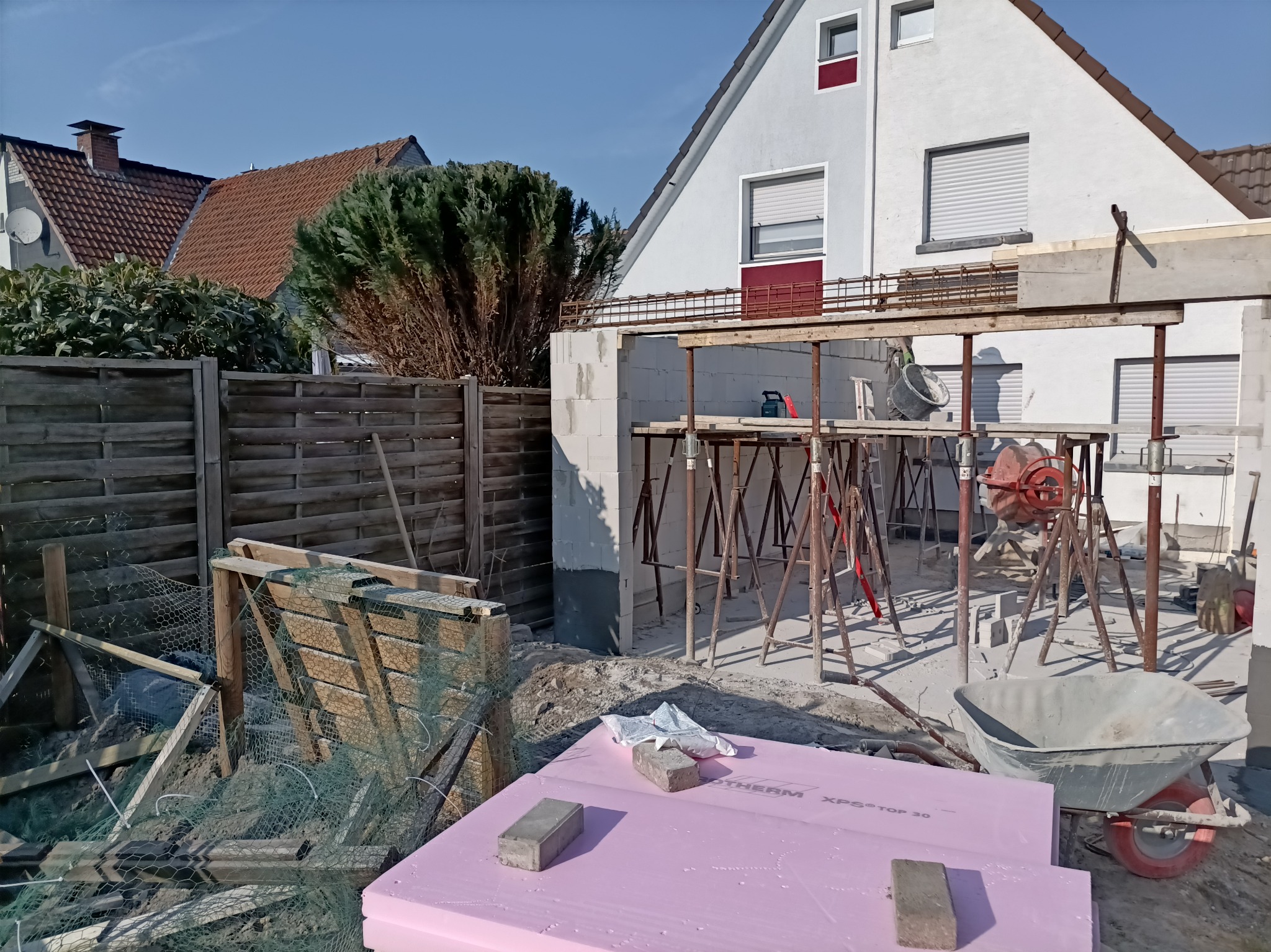 Budowa domu z betonu komórkowego: widoczne rusztowania, bloczki, mieszarka i płyty izolacyjne na tle częściowo wzniesionej konstrukcji.