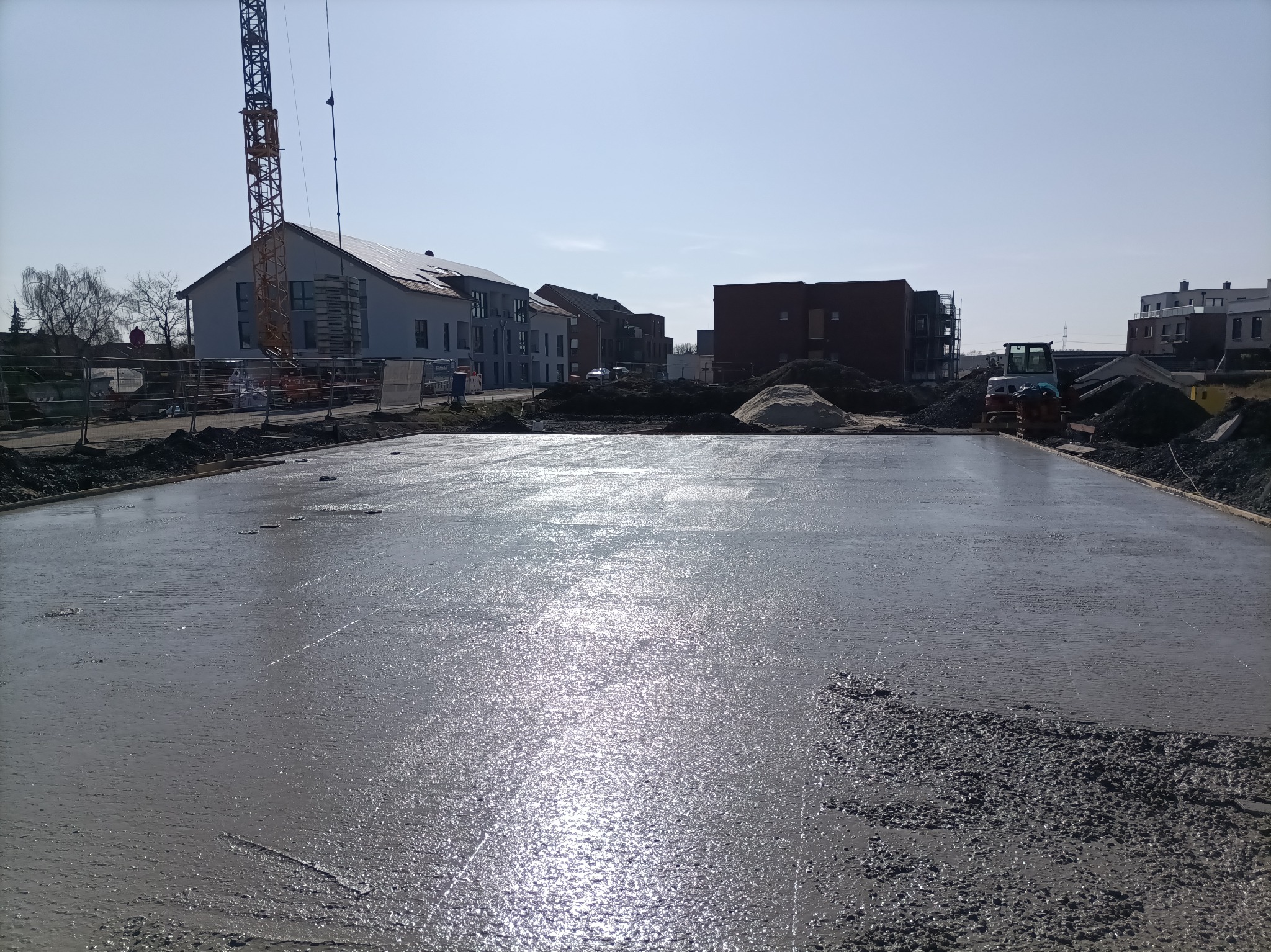 Wylana, świeża płyta fundamentowa pod budowę domu jednorodzinnego, z widocznym żurawiem budowlanym w tle i przygotowanym terenem pod dalsze prace.