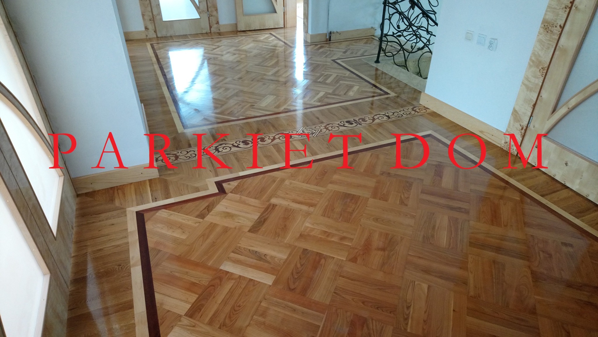 Ułożony parkiet w jodełkę z dekoracyjnym obramowaniem i bordiurą z motywem roślinnym, widoczne przejście do kolejnego pomieszczenia z podobnym wzorem parkietu.