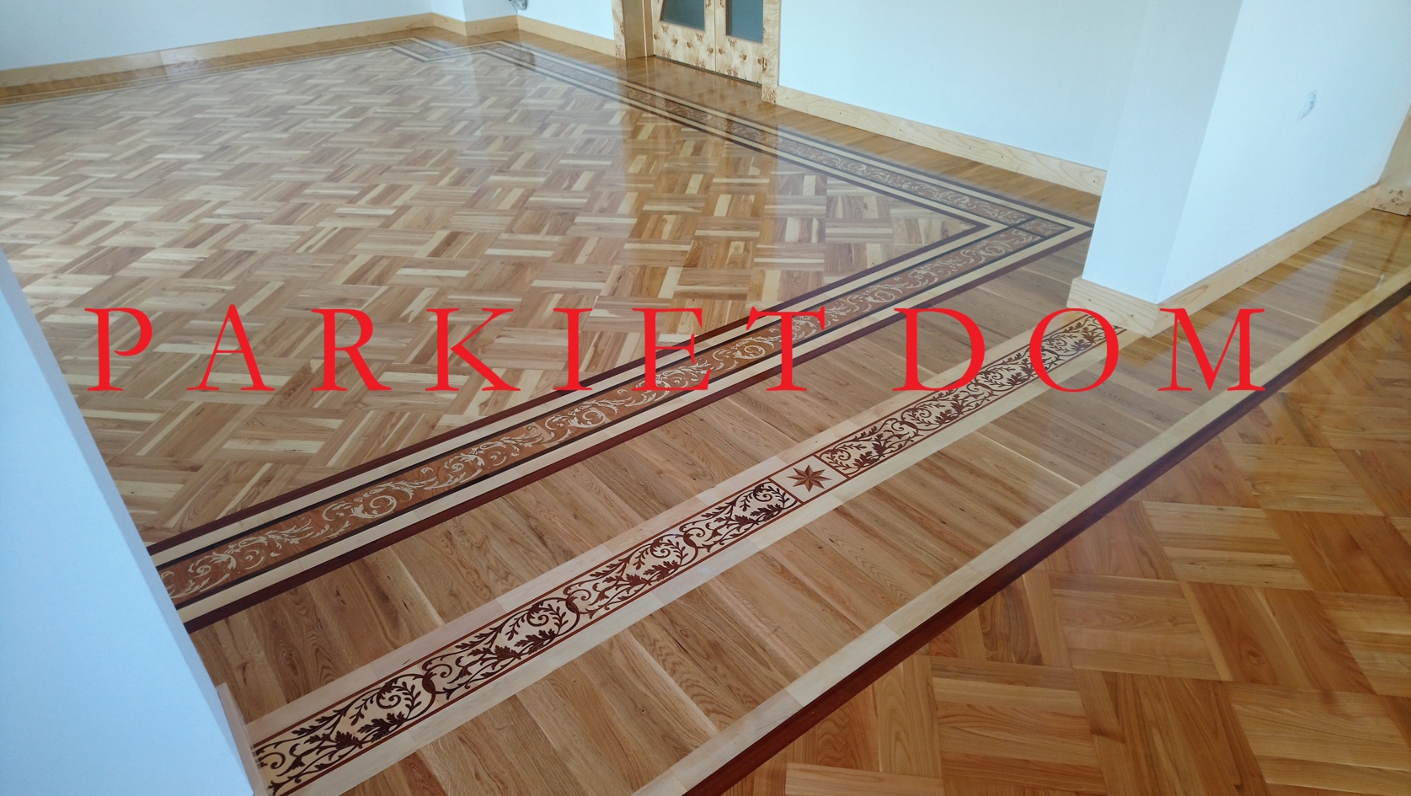 Wypolerowana, jasna podłoga z parkietu ułożonego we wzór szachownicy, obramowana dekoracyjnym pasem z motywami roślinnymi i geometrycznymi.