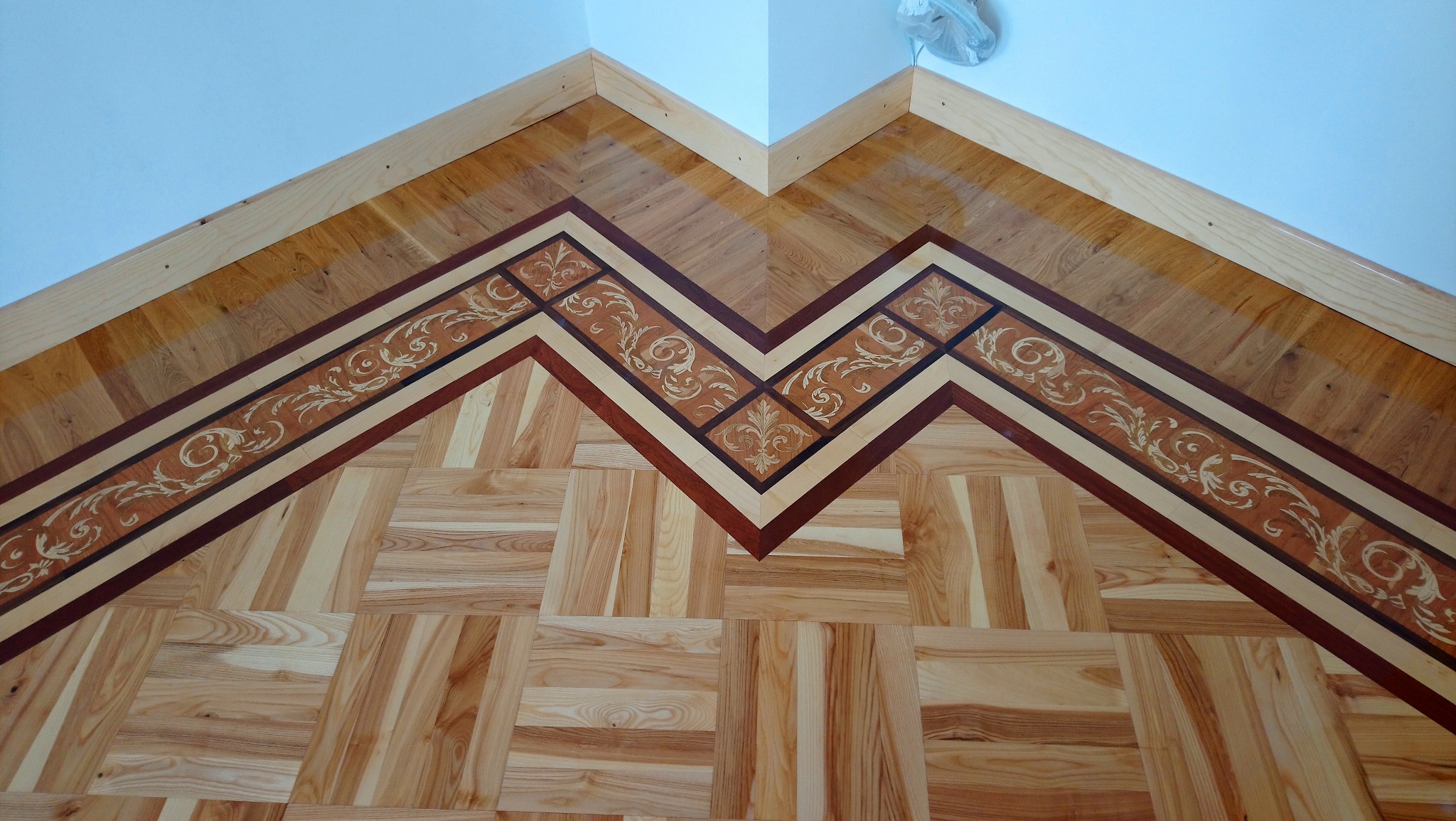 Dekoracyjna podłoga z parkietu w jodełkę z intarsjami i bordiurą w kształcie zygzaka, wykończona listwą przypodłogową.