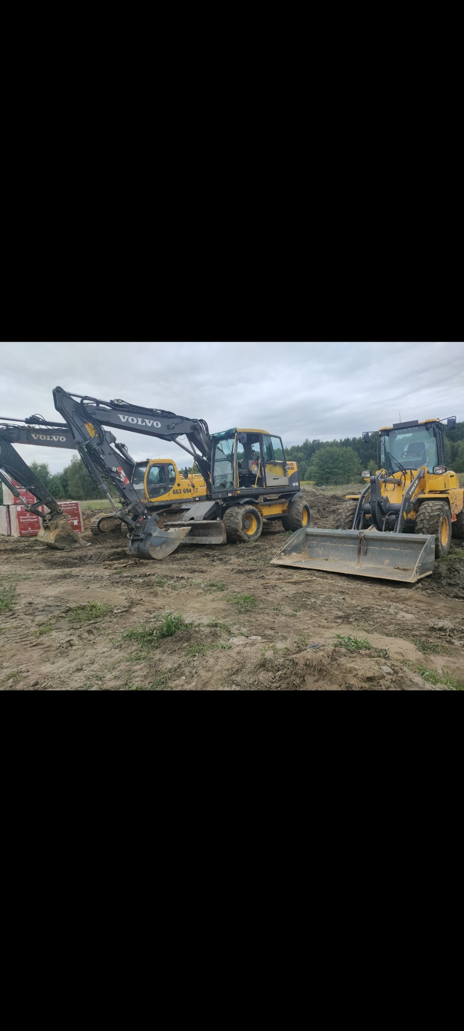 Żółte maszyny budowlane Volvo: koparka kołowa z numerem 663 694 7 i ładowarka kołowa z łyżką na placu budowy.