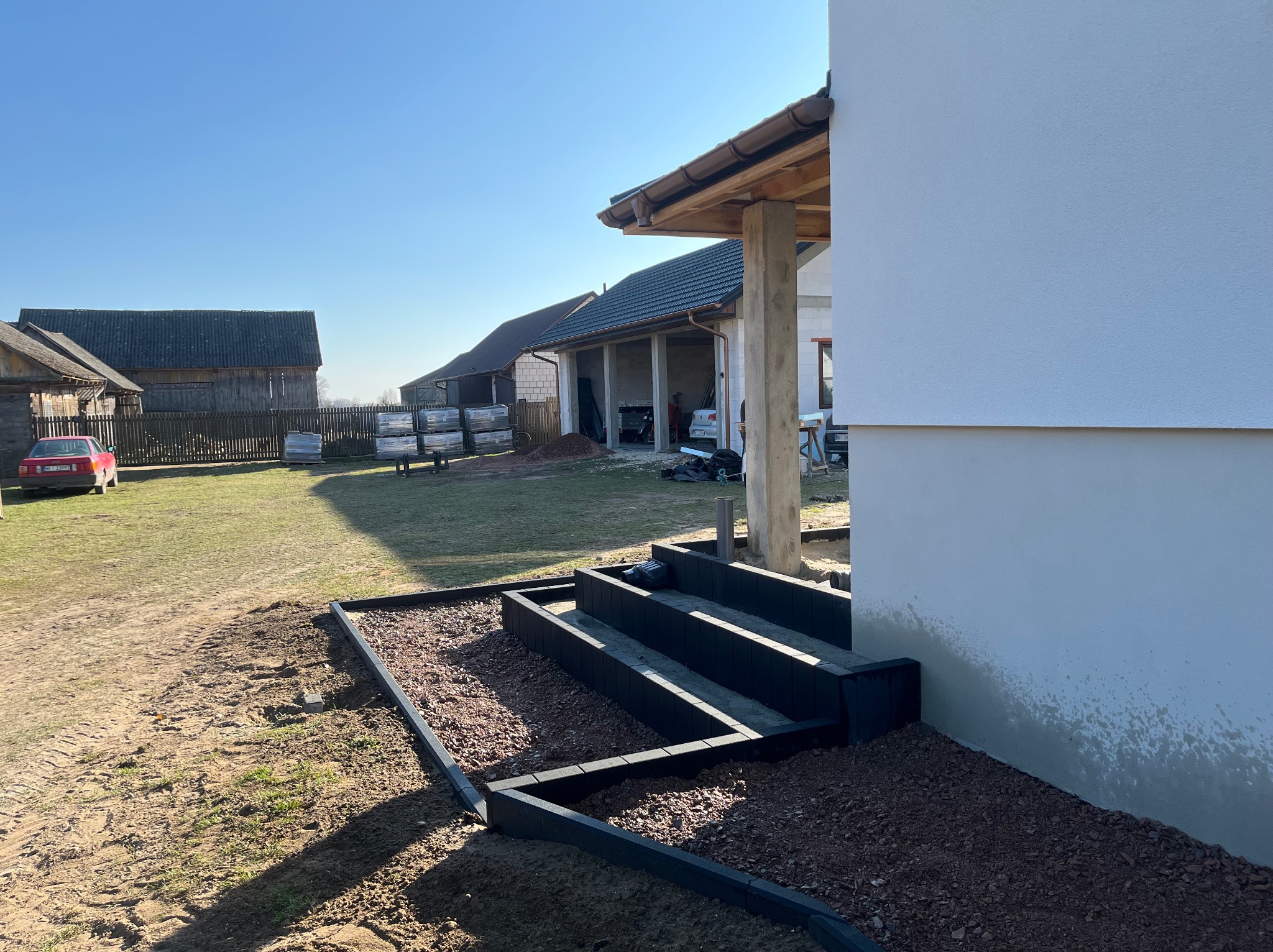 Nowe schody z obrzeżami i wysypanym grysem na posesji, w tle budynki gospodarcze i trawnik. Słoneczny dzień.