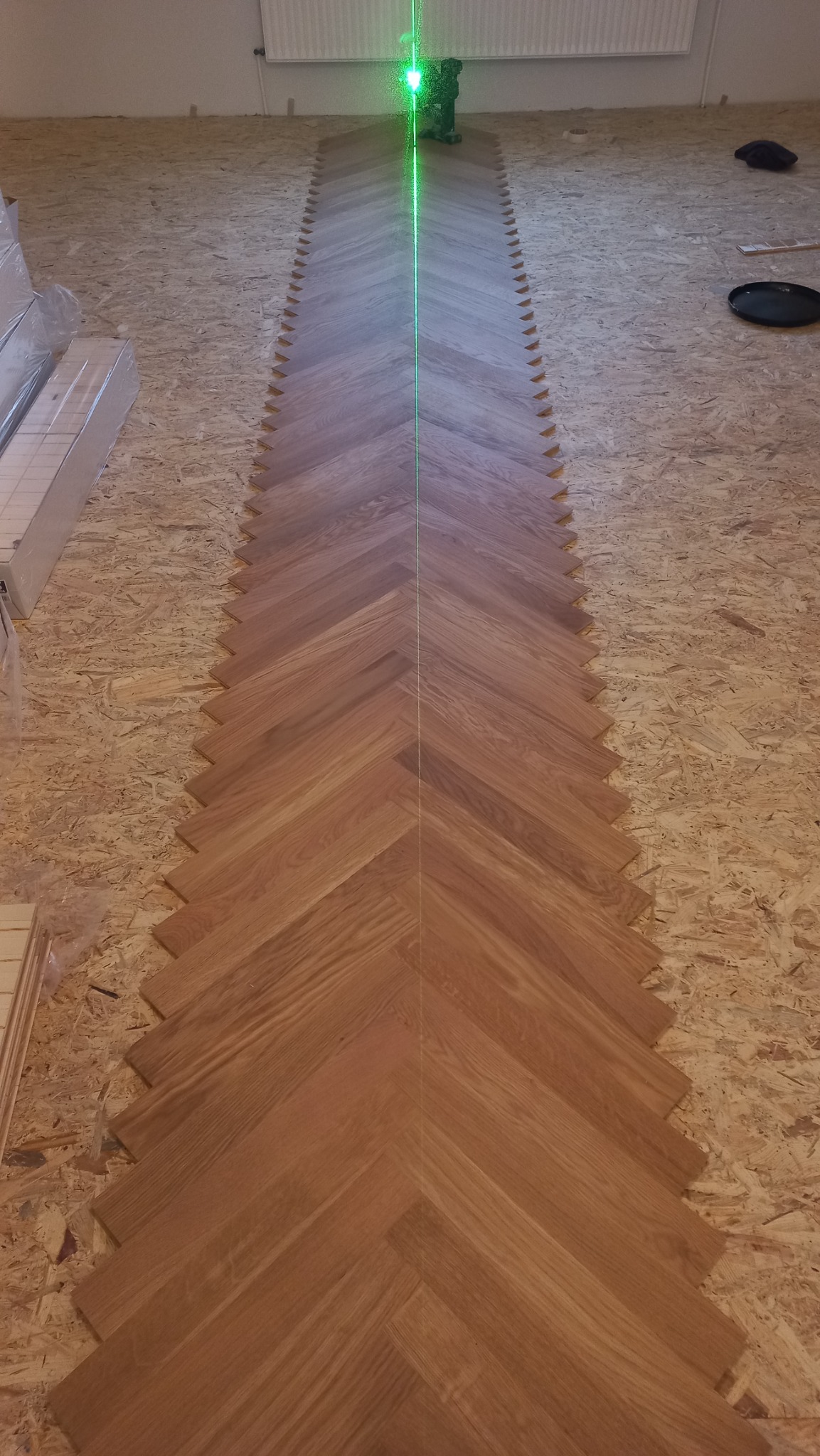 Układanie parkietu w jodełkę, widoczny laser wyznaczający linię prostą, płyty OSB jako podkład.
