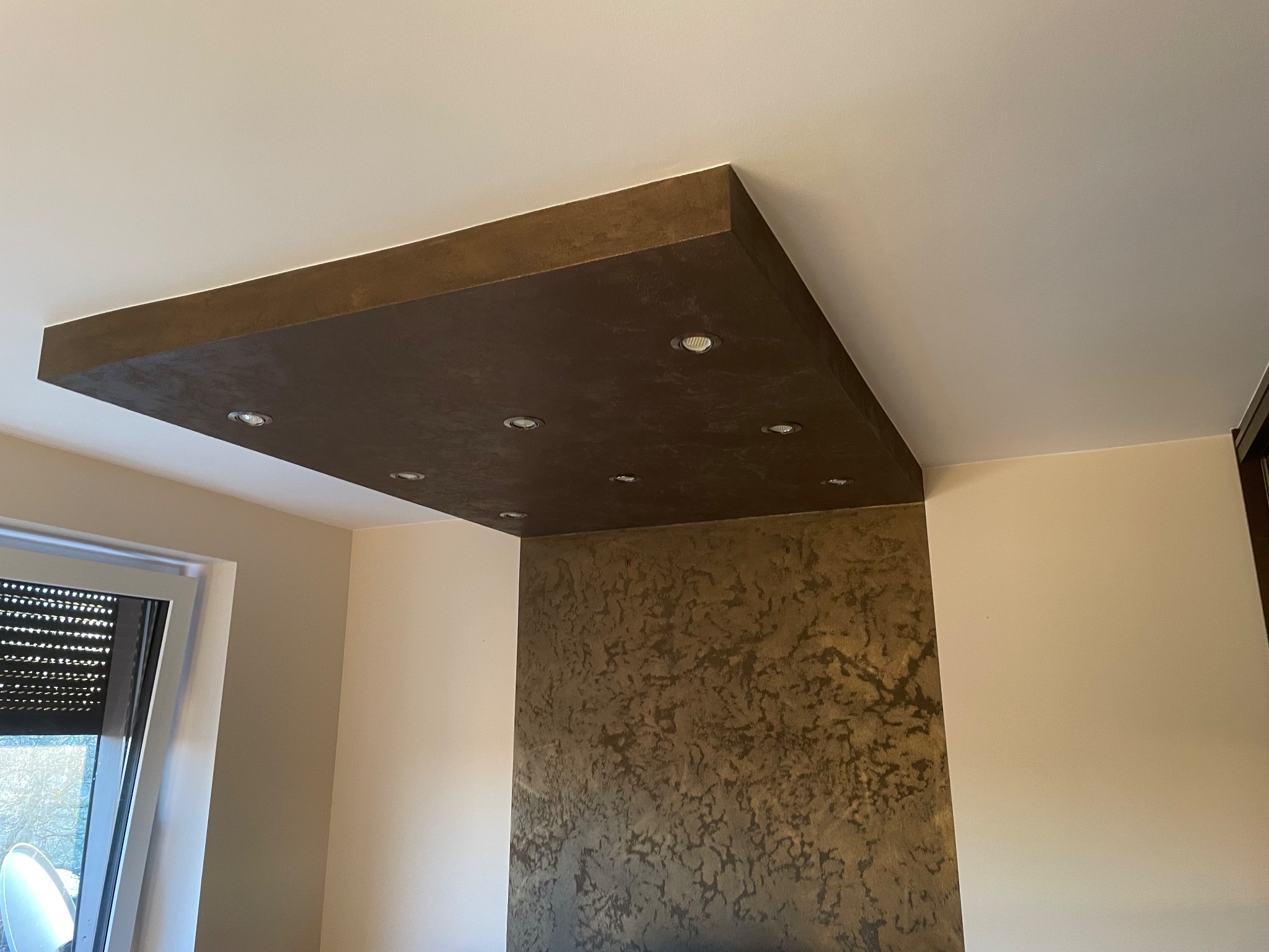 Dekoracyjny sufit podwieszany w kolorze brązu z oświetleniem punktowym i pasująca ściana z dekoracyjną fakturą, widok z dołu.