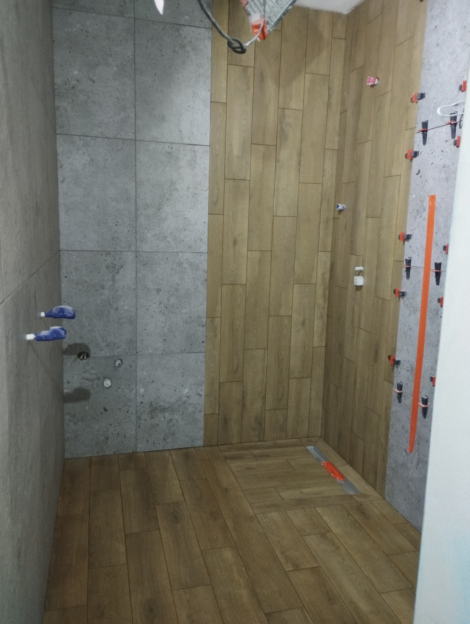 Montaż płytek imitujących drewno na podłodze i ścianie w łazience w Popławach, z widocznymi systemami poziomowania płytek i odpływem liniowym.