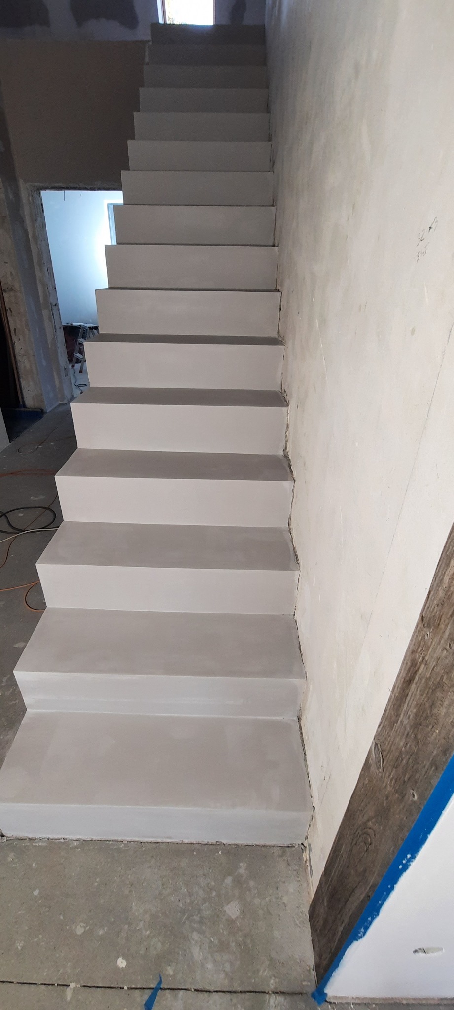 Betonowe schody w trakcie budowy lub remontu, surowe ściany i podłoga, widoczne ślady prac budowlanych.