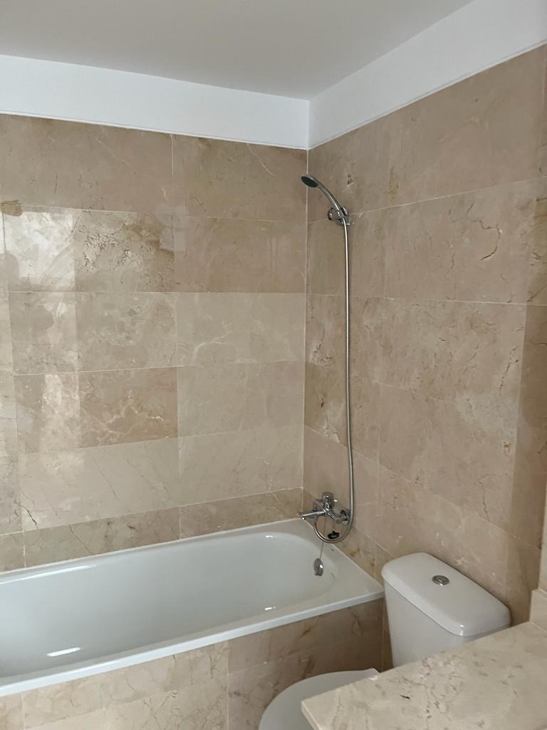 Wykończona łazienka z beżowymi marmurkowymi płytkami, białą wanną i toaletą, chromowaną armaturą prysznicową.