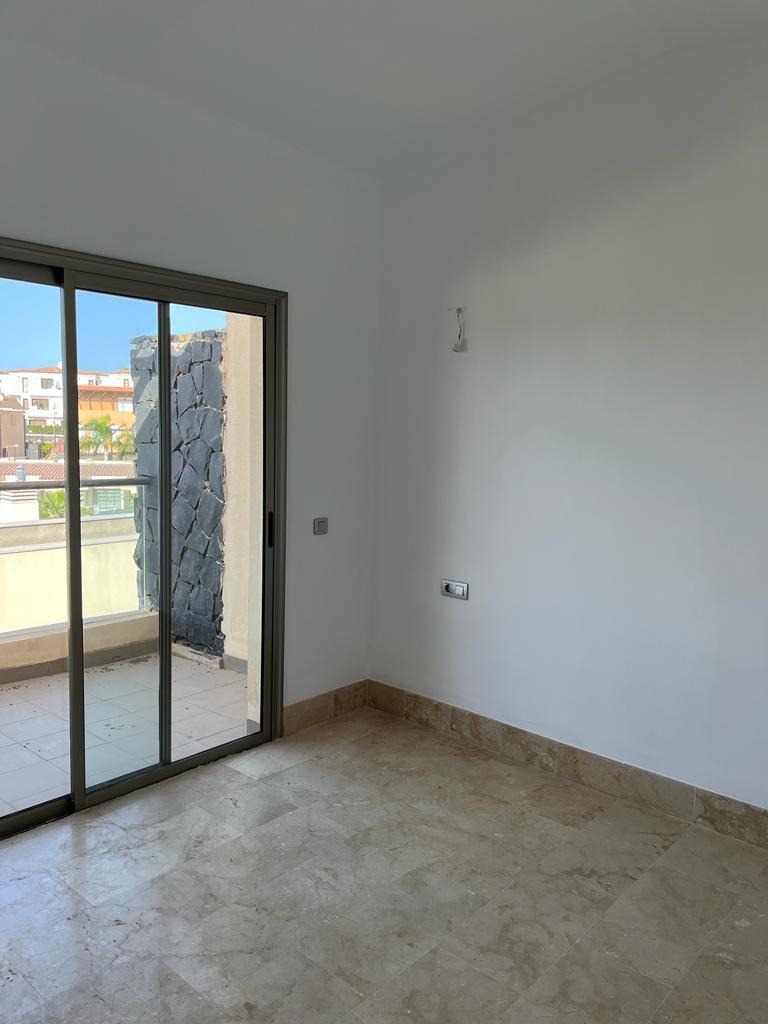 Pusty pokój z marmurową podłogą i wyjściem na balkon z kamienną ścianą, świeżo po malowaniu ścian na biało.