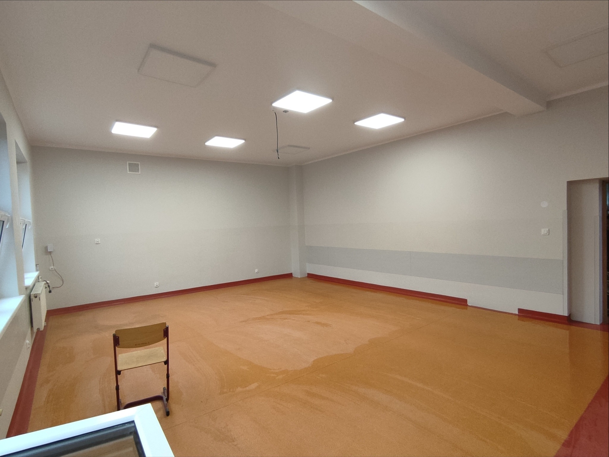Wyremontowana sala edukacyjna z nową podłogą, świeżo pomalowanymi ścianami i nowoczesnym oświetleniem sufitowym. Widoczny pojedynczy szkolny stolik.