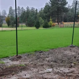 Nowo założony trawnik sportowy w Jarosławiu, z widocznymi słupkami do siatki i fragmentem grząskiego terenu przed trawnikiem.
