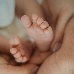 Marlena Jankowska - Delikatne stópki noworodka trzymane w dłoniach rodzica, uchwycone w ciepłym, intymnym ujęciu makro.