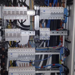 Rozdzielnica elektryczna z zamontowanymi bezpiecznikami i uporządkowanymi przewodami w różnych kolorach, zamocowanymi do szyn DIN.