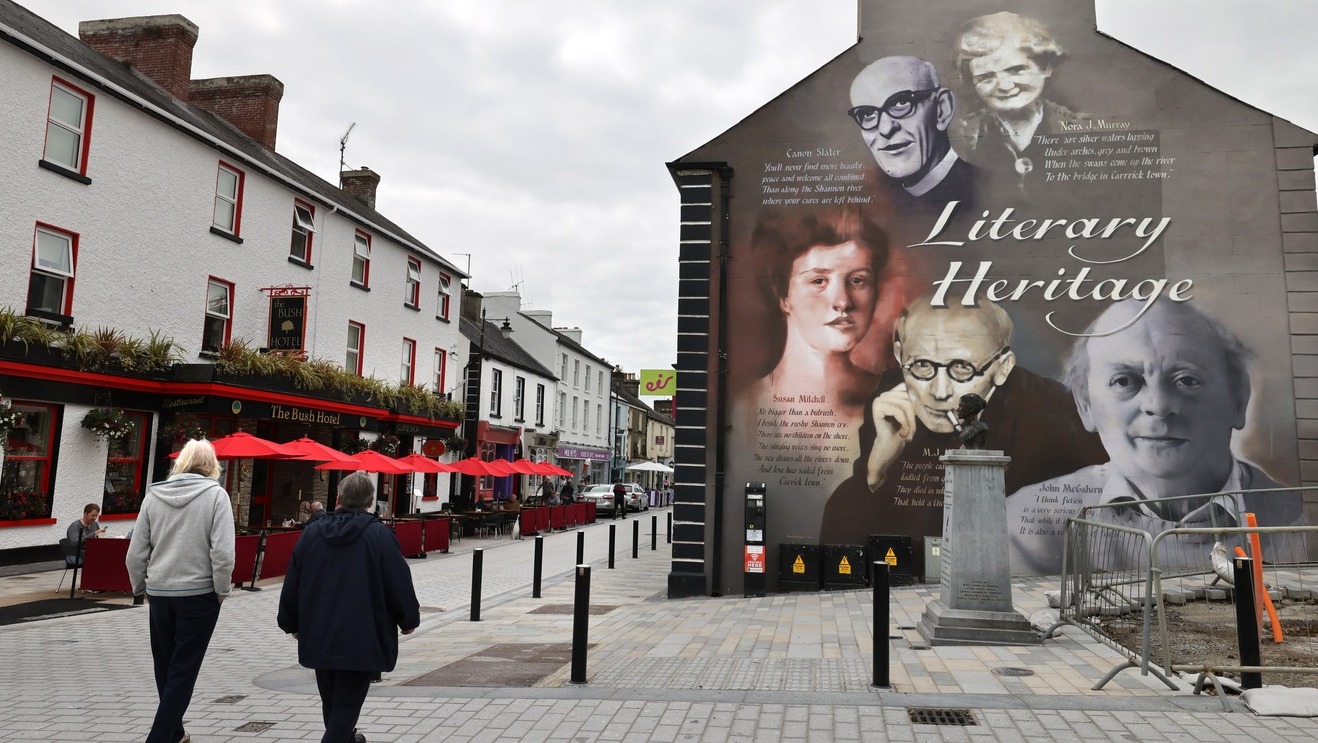 Ulica w Lubinie z nową nawierzchnią z kostki brukowej, widoczne chodniki i jezdnia, na drugim planie budynki z czerwonymi parasolami restauracji.