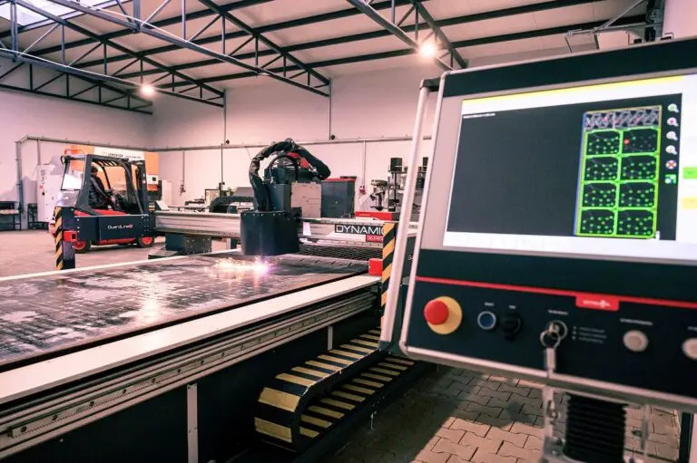 Automatyczne cięcie plazmowe metalu na dużej maszynie CNC z robotycznym ramieniem, widoczny panel sterowania z ekranem i w tle wózek widłowy.