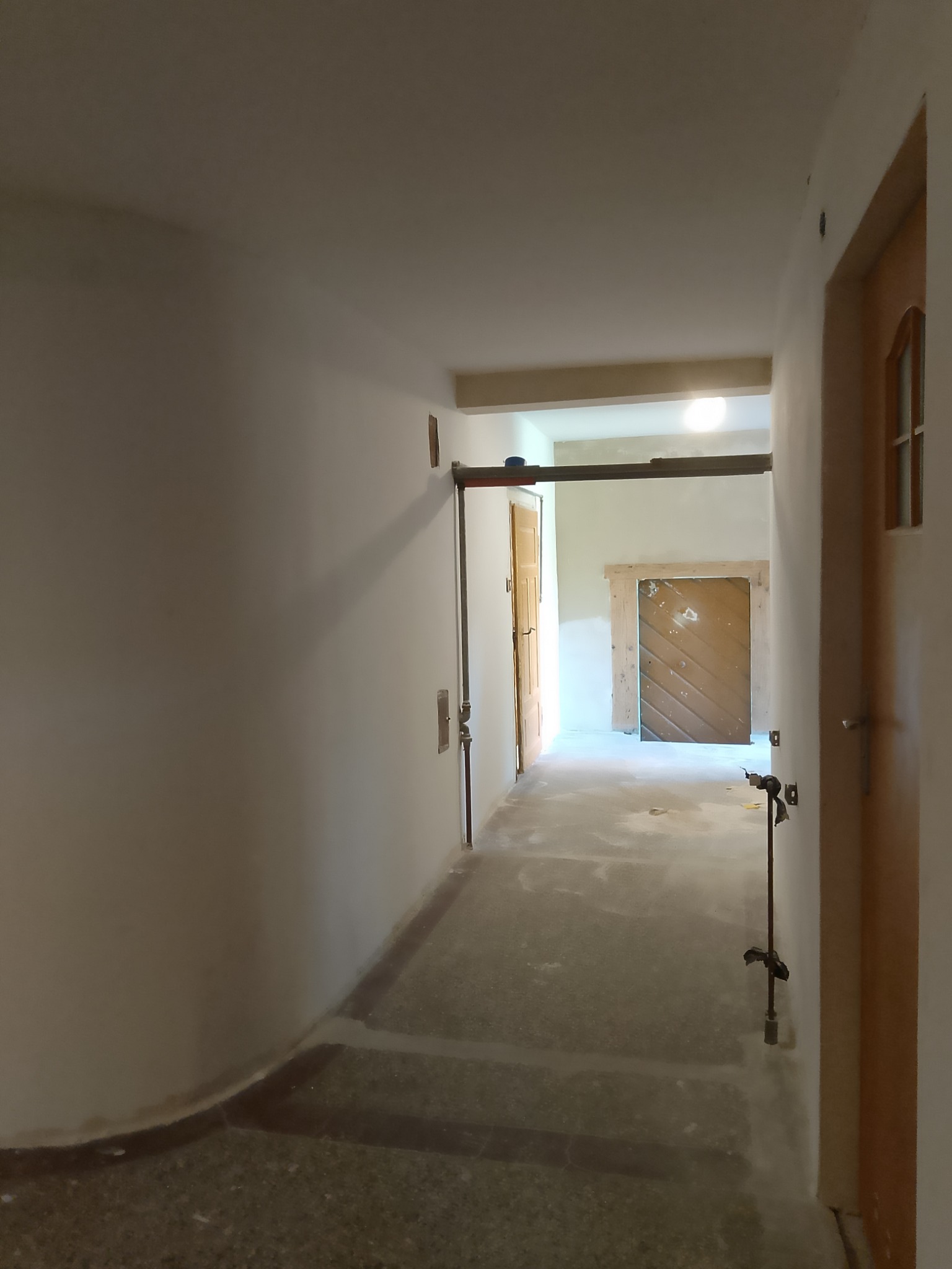 Korytarz w trakcie remontu: widoczne ślady po instalacjach na ścianach, surowy beton na podłodze, przygotowane otwory drzwiowe z widoczną konstrukcją nośną.
