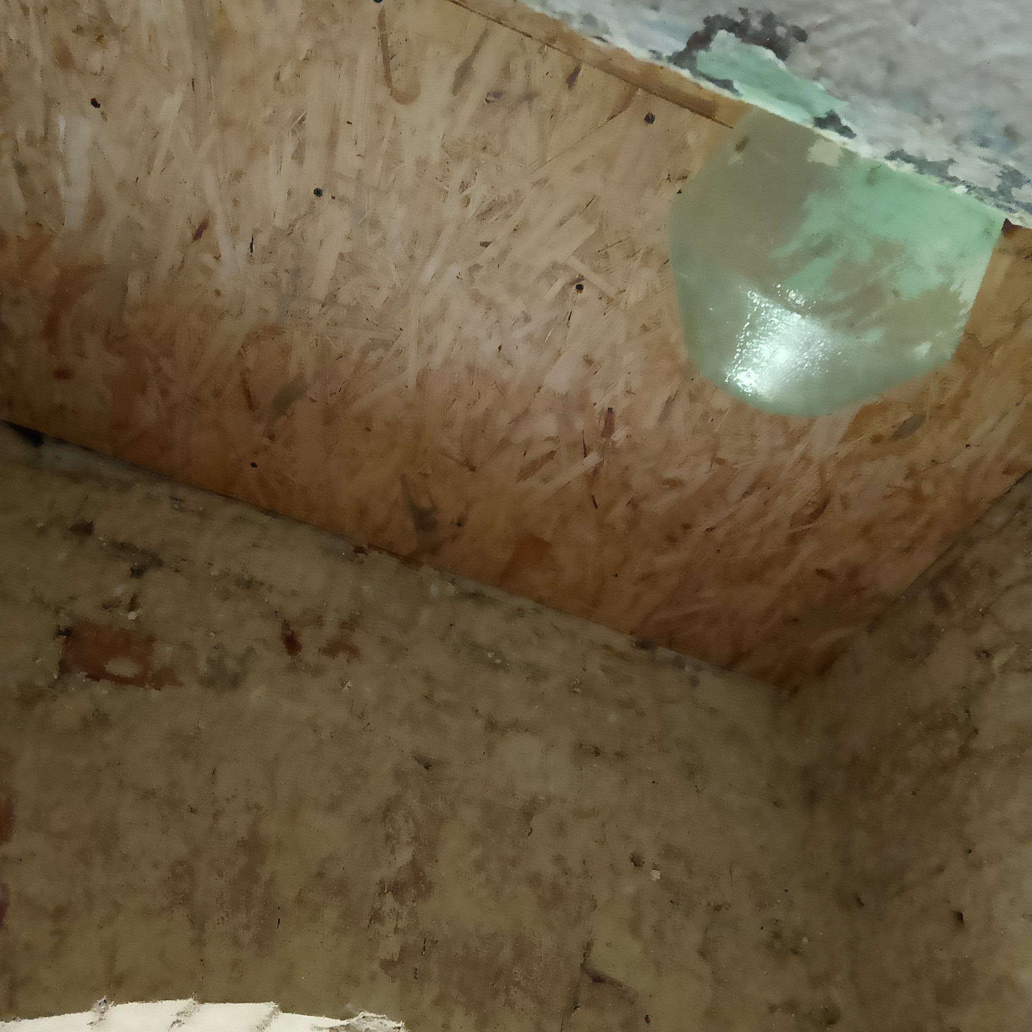 Surowe wnętrze poddasza z widoczną płytą OSB na skosie dachu i fragmentami ocieplenia z folią w narożniku.