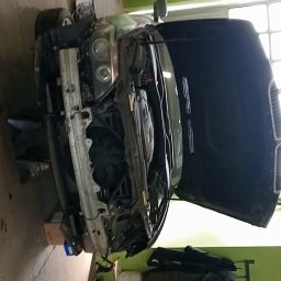 Karol krop - Samochód z otwartą maską w warsztacie, widoczny silnik i elementy przedniego zawieszenia, podnośnik warsztatowy pod autem.