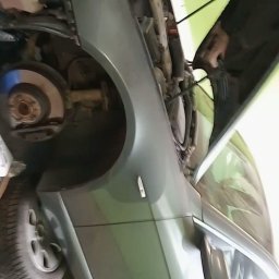 Karol krop - Szary samochód z otwartą maską, widoczny fragment koła, błotnik i wnętrze komory silnika w warsztacie.