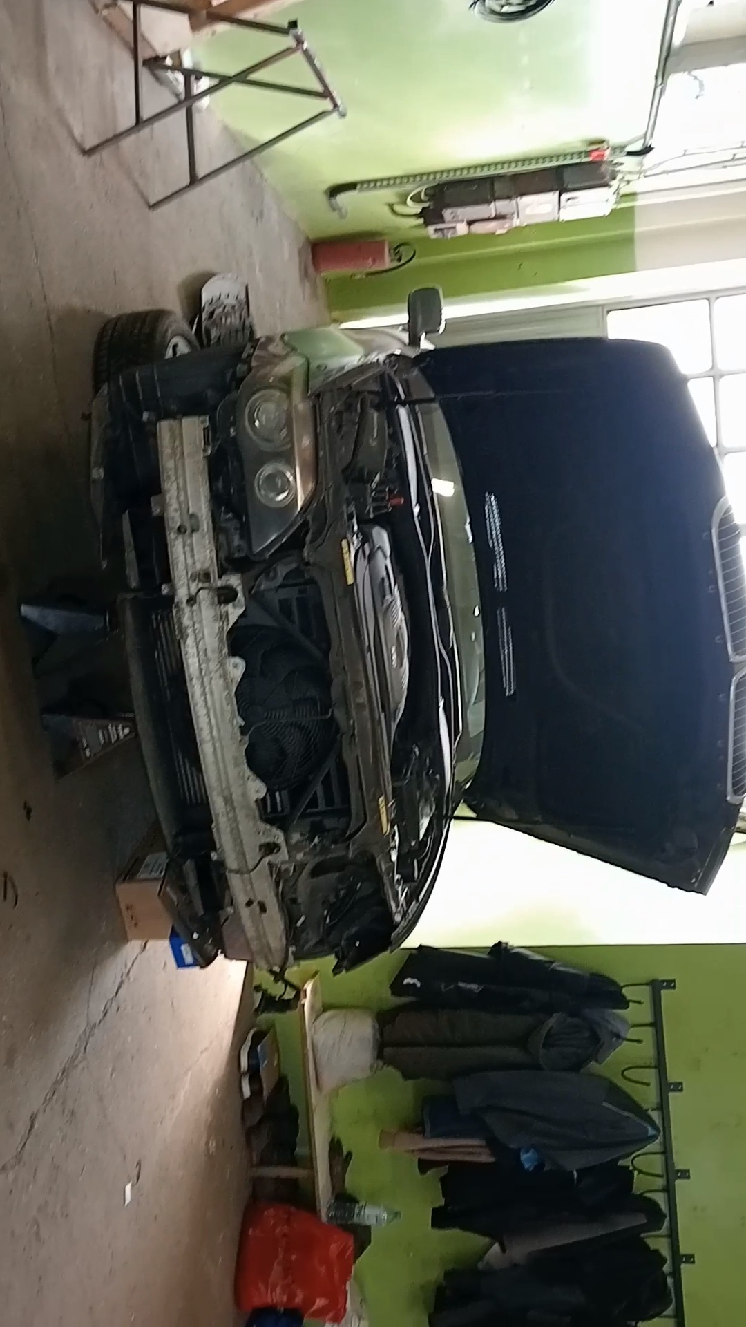 Samochód z otwartą maską w warsztacie, widoczny silnik i elementy przedniego zawieszenia, podnośnik warsztatowy pod autem.