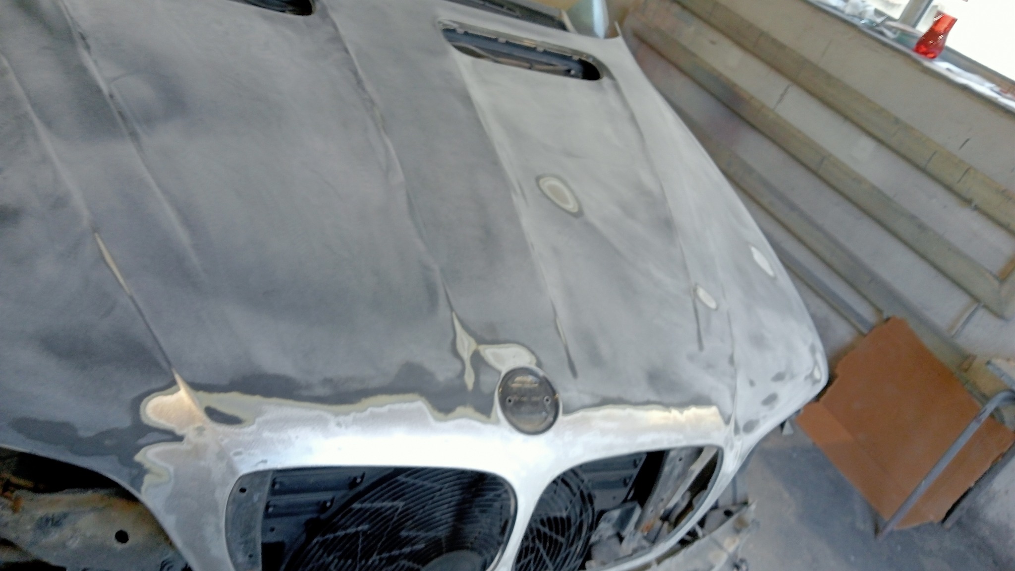 Przygotowany do lakierowania przód samochodu z widocznymi warstwami szpachli i podkładu, zdemontowane elementy, ujęcie z góry.