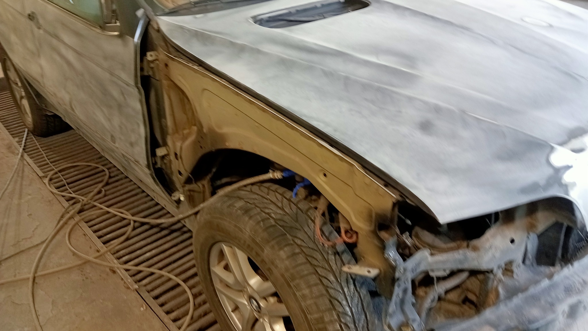 Samochód w trakcie naprawy blacharskiej, z elementami zdemontowanymi i powierzchnią przygotowaną pod lakierowanie, widoczne ślady szlifowania i szpachlowania na karoserii.