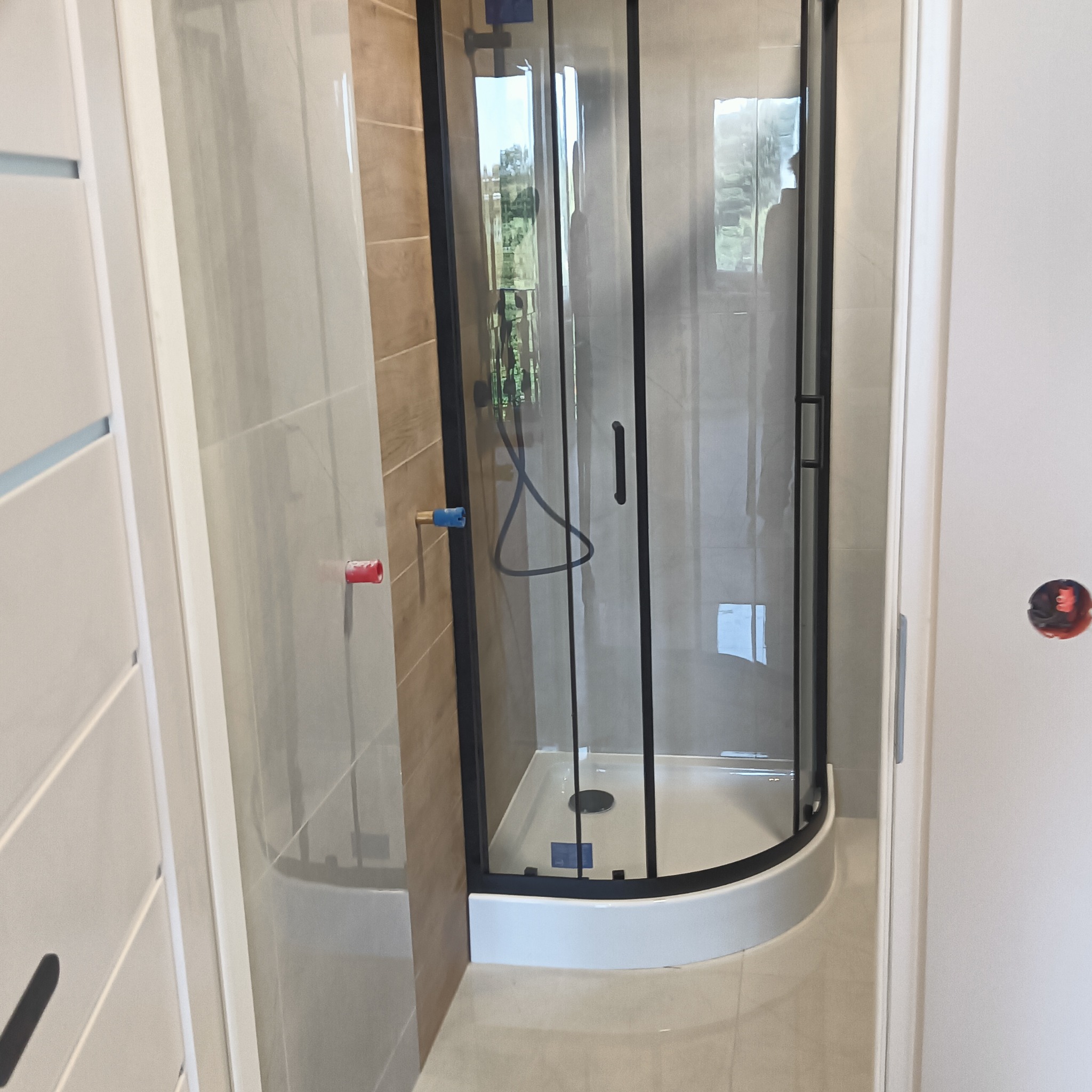 Nowoczesna kabina prysznicowa z czarną ramą, widoczna w wykończonej łazience z beżowymi płytkami i białą armaturą. Minimalistyczny design, świeżo po montażu.