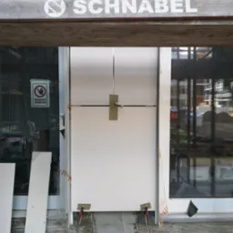 Montaż białej płyty warstwowej w nowym budynku, widoczne narzędzia, znak zakazu wstępu na szybie, element drewniany z napisem 'SCHNABEL' u góry.