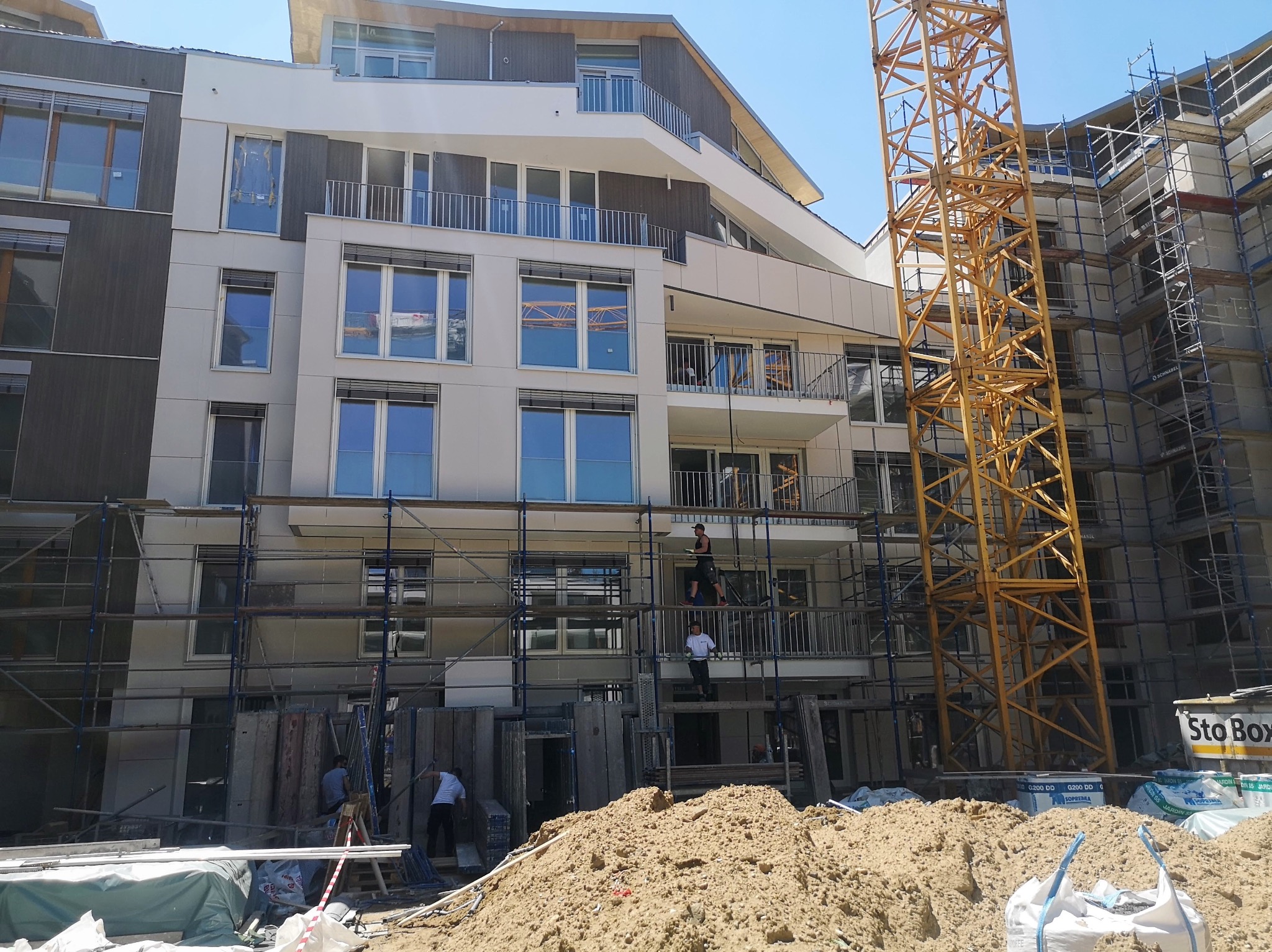 Wielopiętrowy budynek mieszkalny w trakcie budowy, widoczne rusztowania, dźwig i pracujący robotnicy.