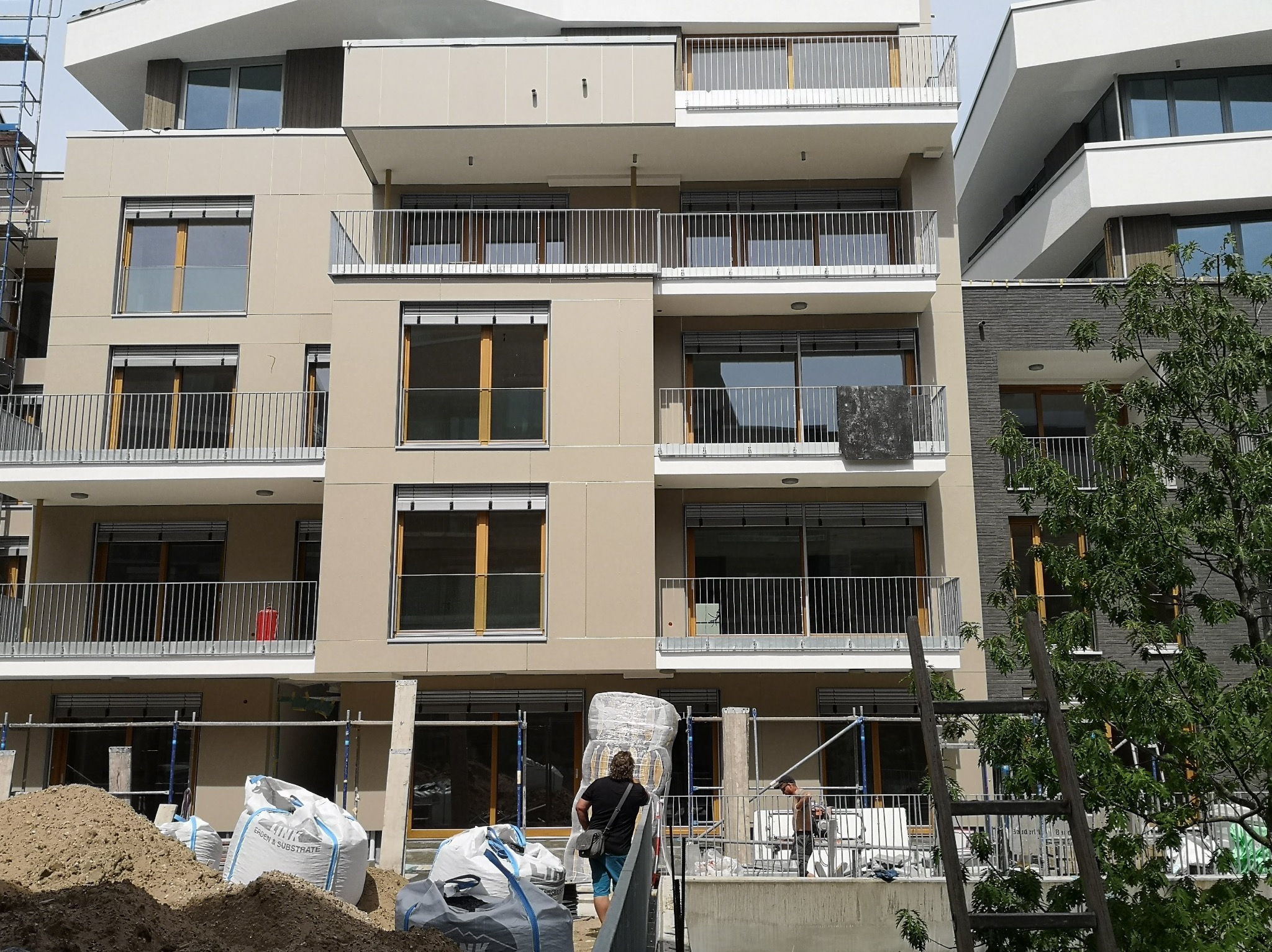 Wielopiętrowy budynek w trakcie montażu płyt warstwowych, widoczne rusztowania, materiały budowlane i pracownicy