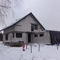 Domki z Mazur - Budowa domu z betonu komórkowego w zimowej scenerii. Widoczne palety z materiałem i ogrodzenie z drewnianych słupków. Część okien zabezpieczona folią.