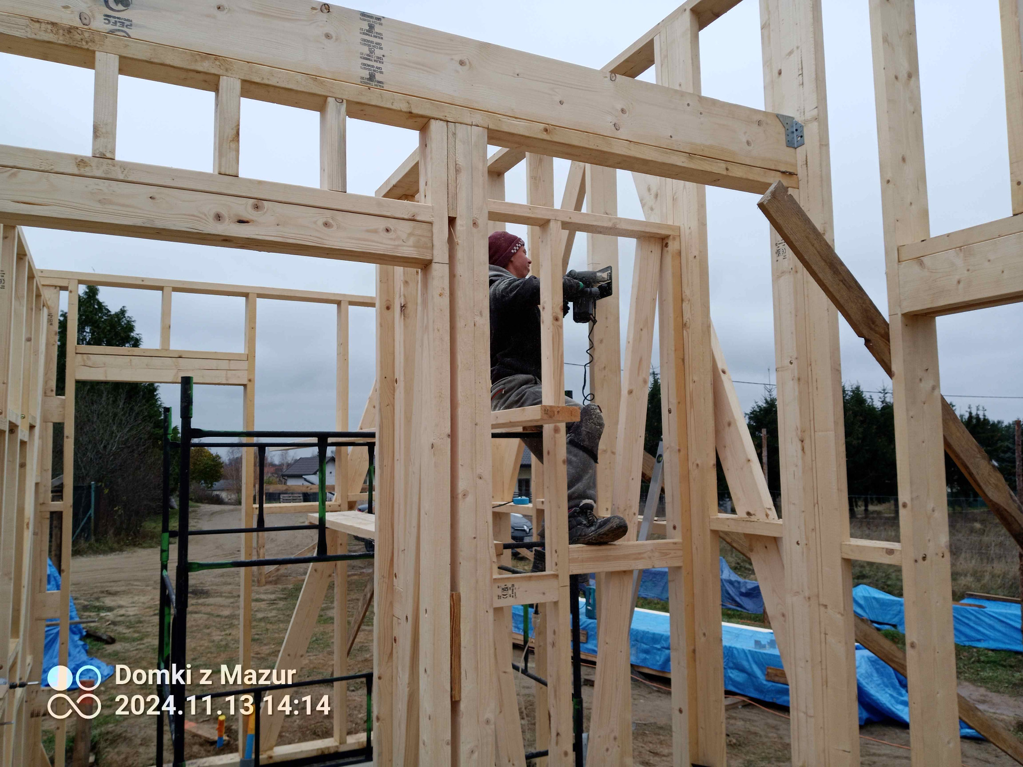 Montera w trakcie budowy domu szkieletowego. Widoczna drewniana konstrukcja, elementy złączone metalowymi łącznikami. Praca na wysokości.