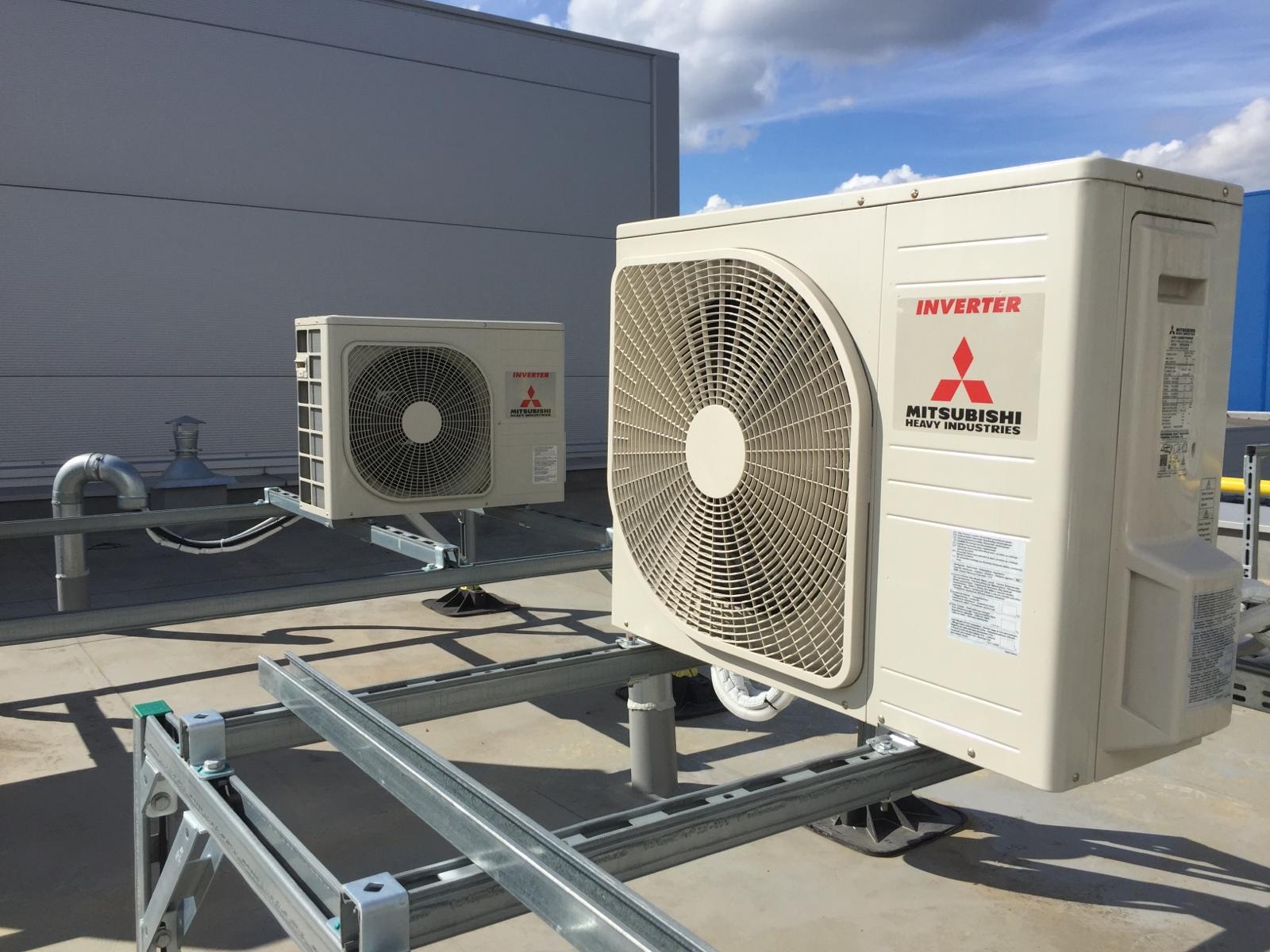 Dwa zewnętrzne moduły klimatyzacyjne Mitsubishi Heavy Industries zamontowane na metalowej konstrukcji wsporczej na dachu budynku przemysłowego, widoczne elementy instalacji wentylacyjnej.