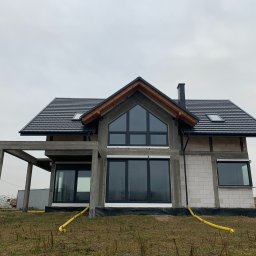 F.H.U RES DOM TOMASZ ZIARNIK - Dom w stanie surowym zamkniętym z zamontowanymi oknami z czarnymi ramami i dachem z dachówki. Budynek z białego bloczka z widoczną konstrukcją betonową.