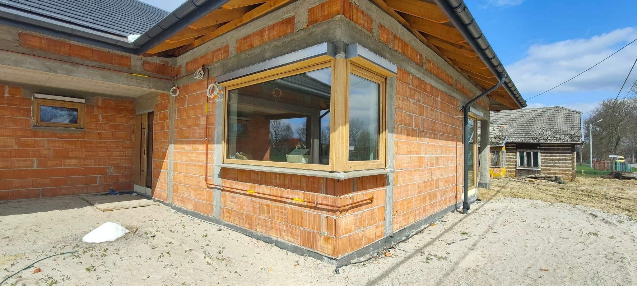 Surowy stan budynku w Rzeszowie z zamontowanymi oknami z naturalnego drewna, widoczne przewody elektryczne i niezabezpieczone mury z cegły.