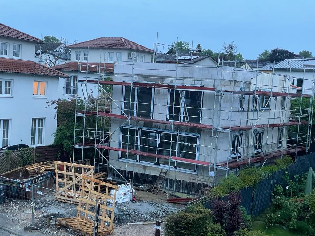 Budowa domu jednorodzinnego w trakcie montażu stolarki okiennej, widoczne rusztowania i materiały budowlane.