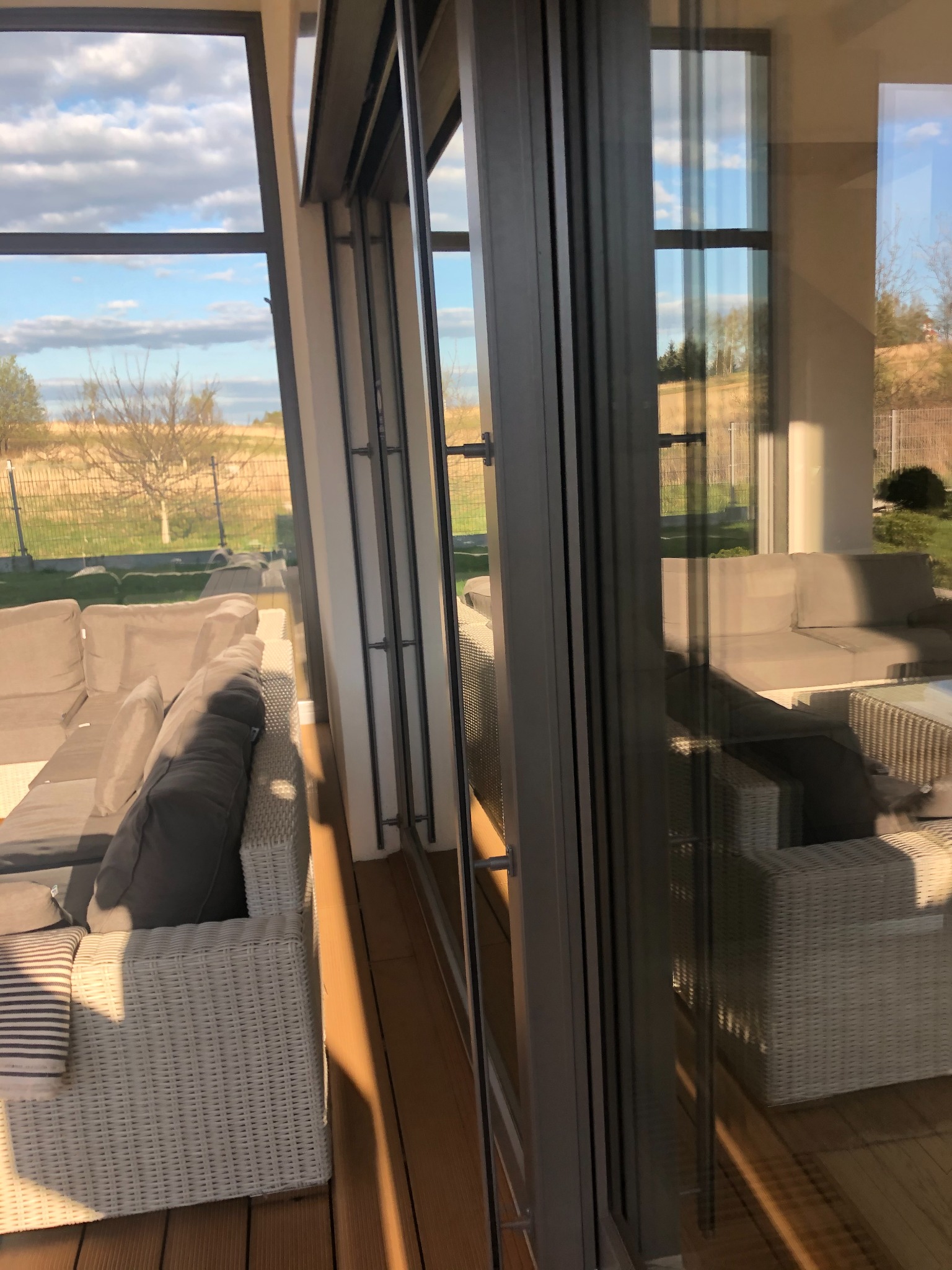 Rozsuwane drzwi tarasowe aluminiowe z widokiem na ogród i meble ogrodowe, z wyraźnymi refleksami na szkle.